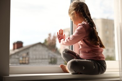 Photo of Orphanage concept. Sad girl sitting on windowsill indoors