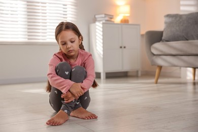 Photo of Orphanage concept. Sad girl sitting on floor indoors