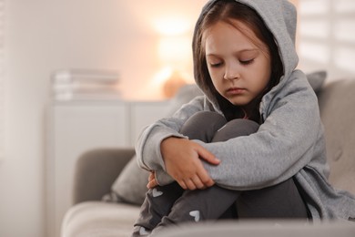 Photo of Orphanage concept. Sad girl sitting on sofa indoors