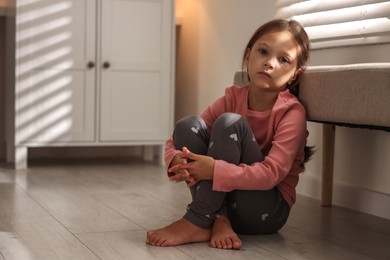 Orphanage concept. Sad girl sitting on floor indoors