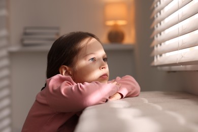 Photo of Orphanage concept. Sad girl and looking through window blinds indoors