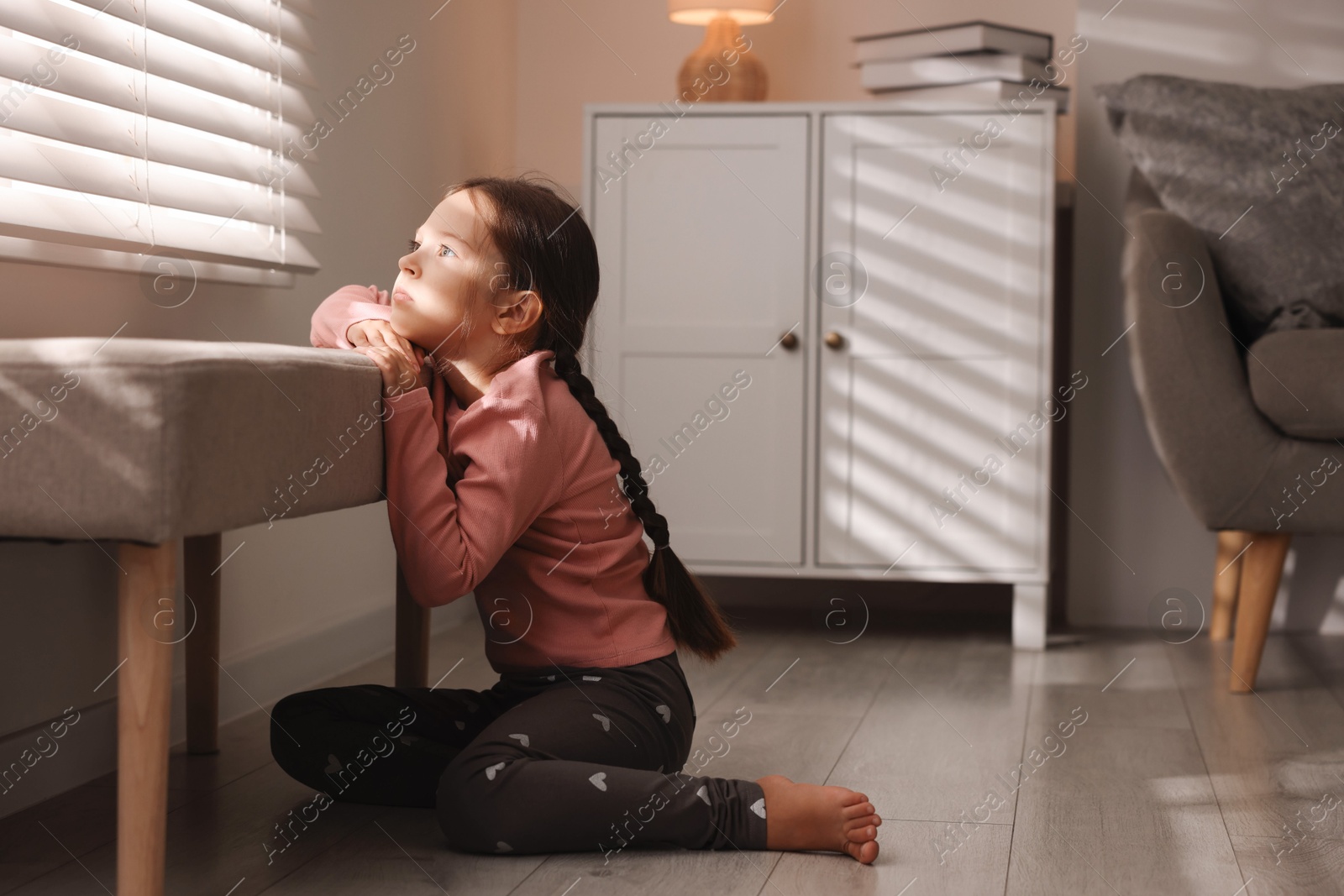 Photo of Orphanage concept. Sad girl and looking through window blinds indoors