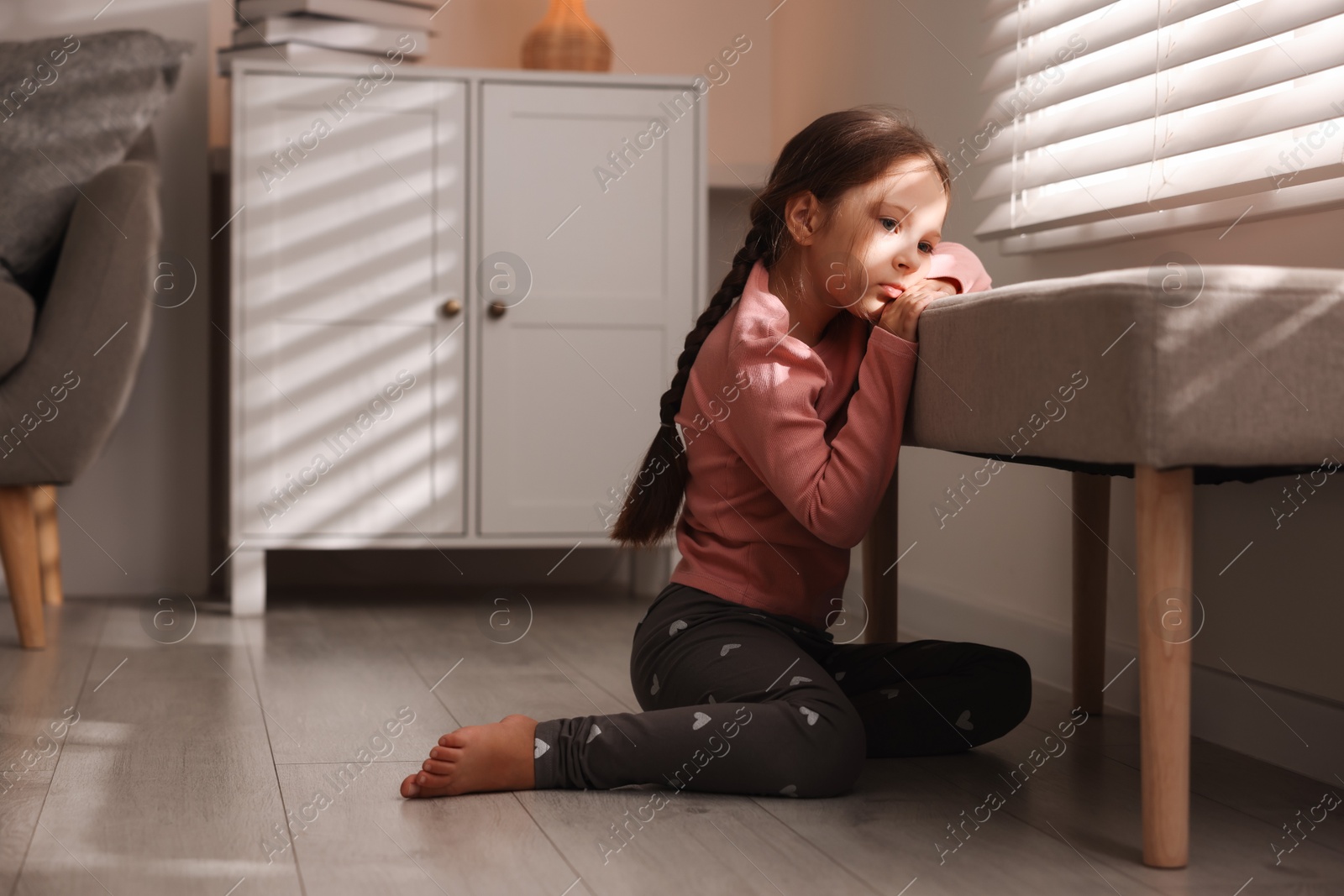 Photo of Orphanage concept. Sad girl and looking through window blinds indoors