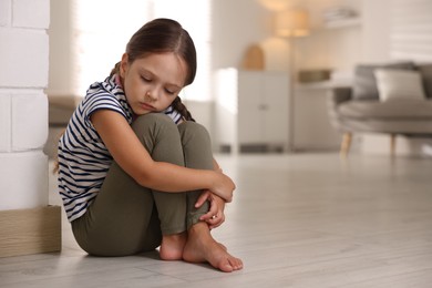 Photo of Orphanage concept. Sad girl sitting on floor indoors