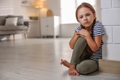 Photo of Orphanage concept. Sad girl sitting on floor indoors