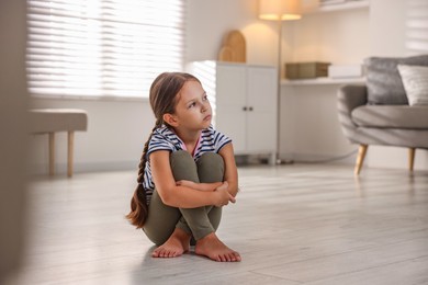 Orphanage concept. Sad girl sitting on floor indoors