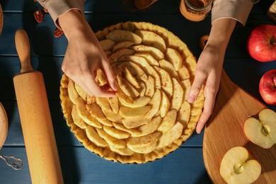 Photo of Woman making homemade apple pie and ingredients on blue wooden table, top view