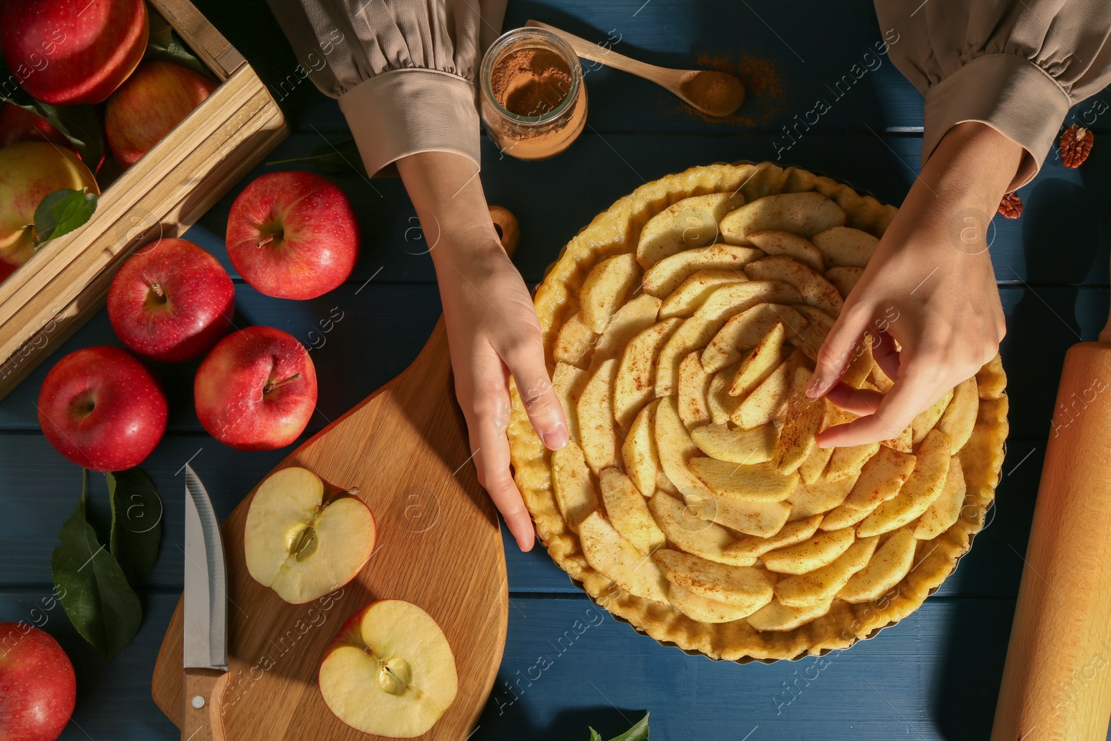 Photo of Woman making homemade apple pie and ingredients on blue wooden table, top view