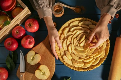 Photo of Woman making homemade apple pie and ingredients on blue wooden table, top view