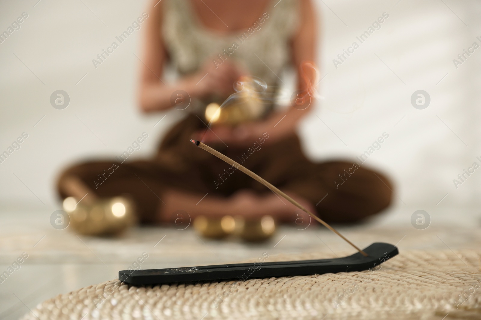 Photo of Incense stick smoldering in holder on wicker mat indoors, selective focus