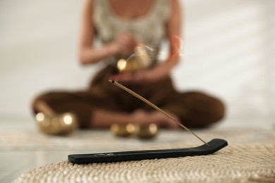 Photo of Incense stick smoldering in holder on wicker mat indoors, selective focus