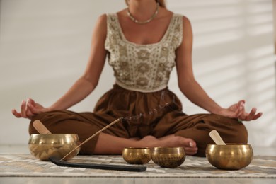 Photo of Young woman with smoldering incense stick and tibetan singing bowls practicing yoga on floor indoors, selective focus