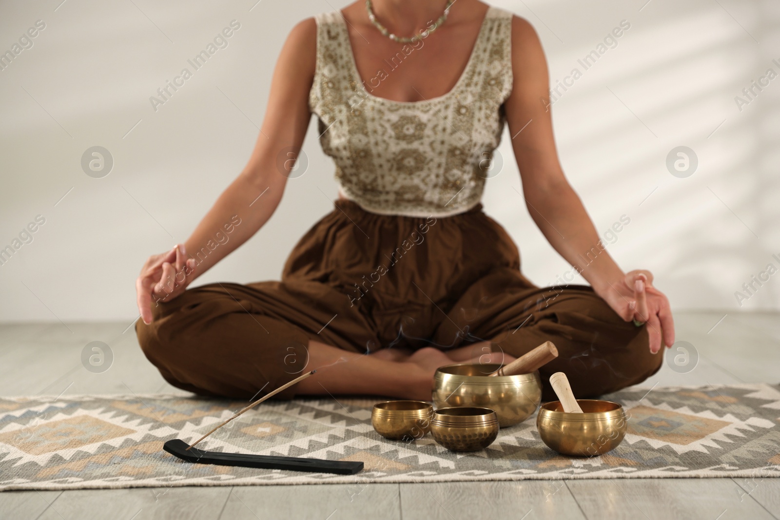 Photo of Young woman with smoldering incense stick and tibetan singing bowls practicing yoga on floor indoors, closeup