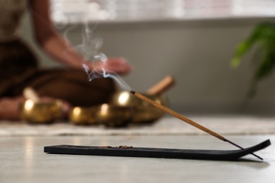 Photo of Incense stick smoldering in holder on floor indoors, selective focus