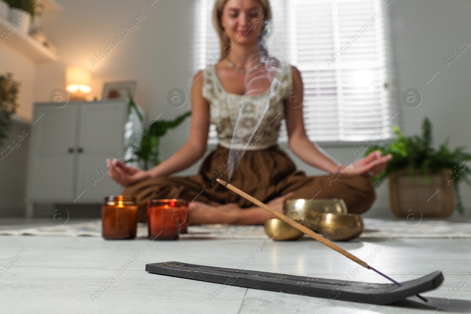 Photo of Young woman practicing yoga on floor indoors, focus on smoldering incense stick