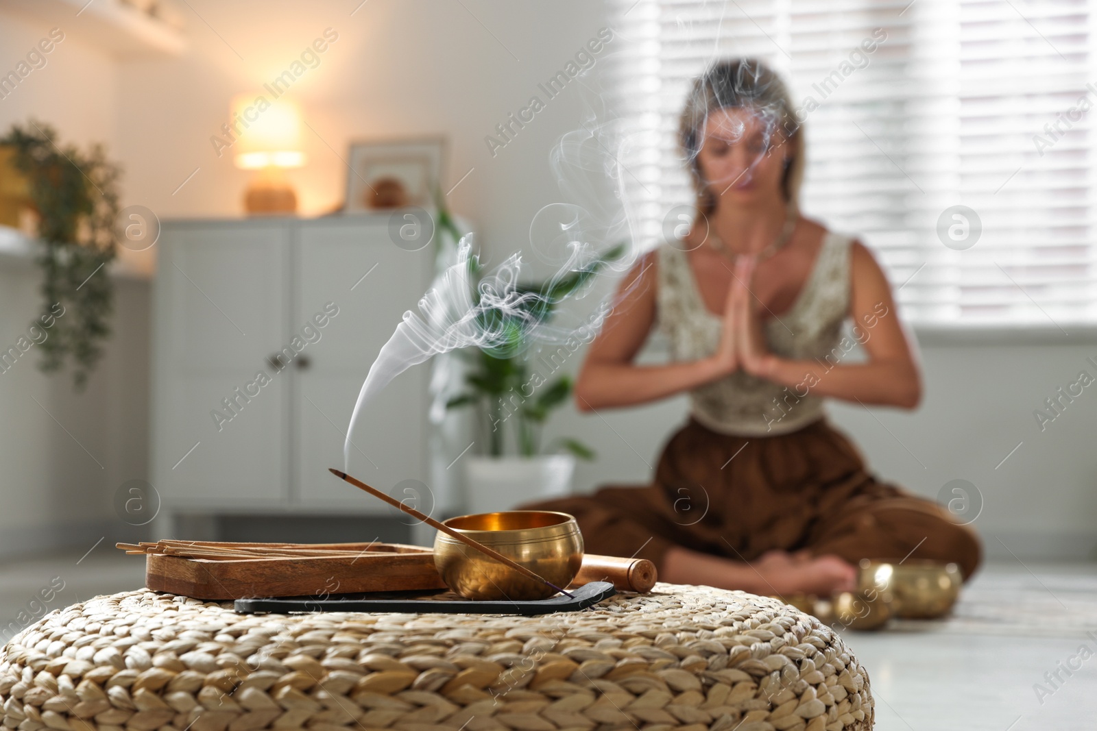 Photo of Young woman practicing yoga indoors, focus on smoldering incense stick and tibetan singing bowl