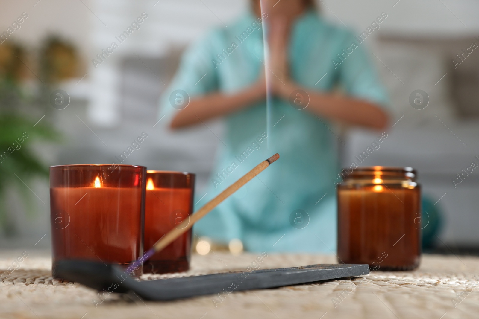 Photo of Incense stick smoldering in holder and burning candles on wicker mat indoors, selective focus