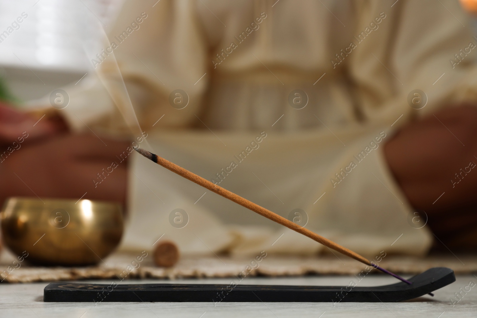 Photo of Incense stick smoldering in holder on floor indoors, selective focus