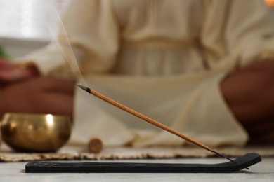 Photo of Incense stick smoldering in holder on floor indoors, selective focus