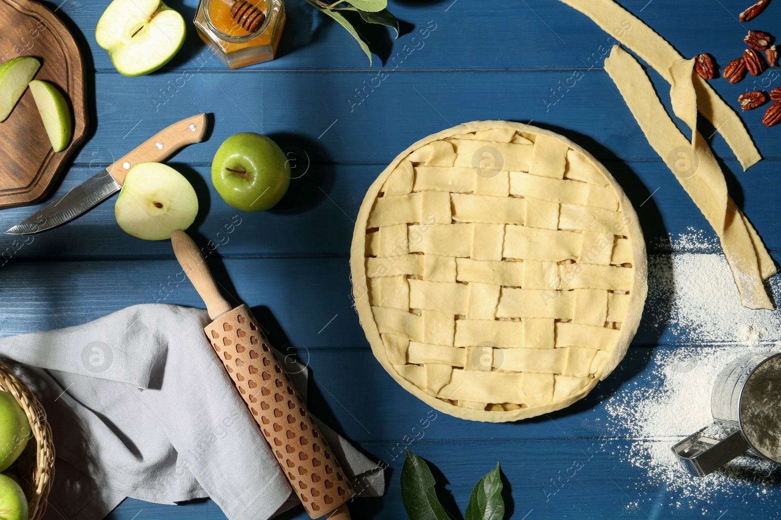 Photo of Uncooked homemade apple pie and ingredients on blue wooden table, flat lay