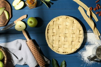 Photo of Uncooked homemade apple pie and ingredients on blue wooden table, flat lay