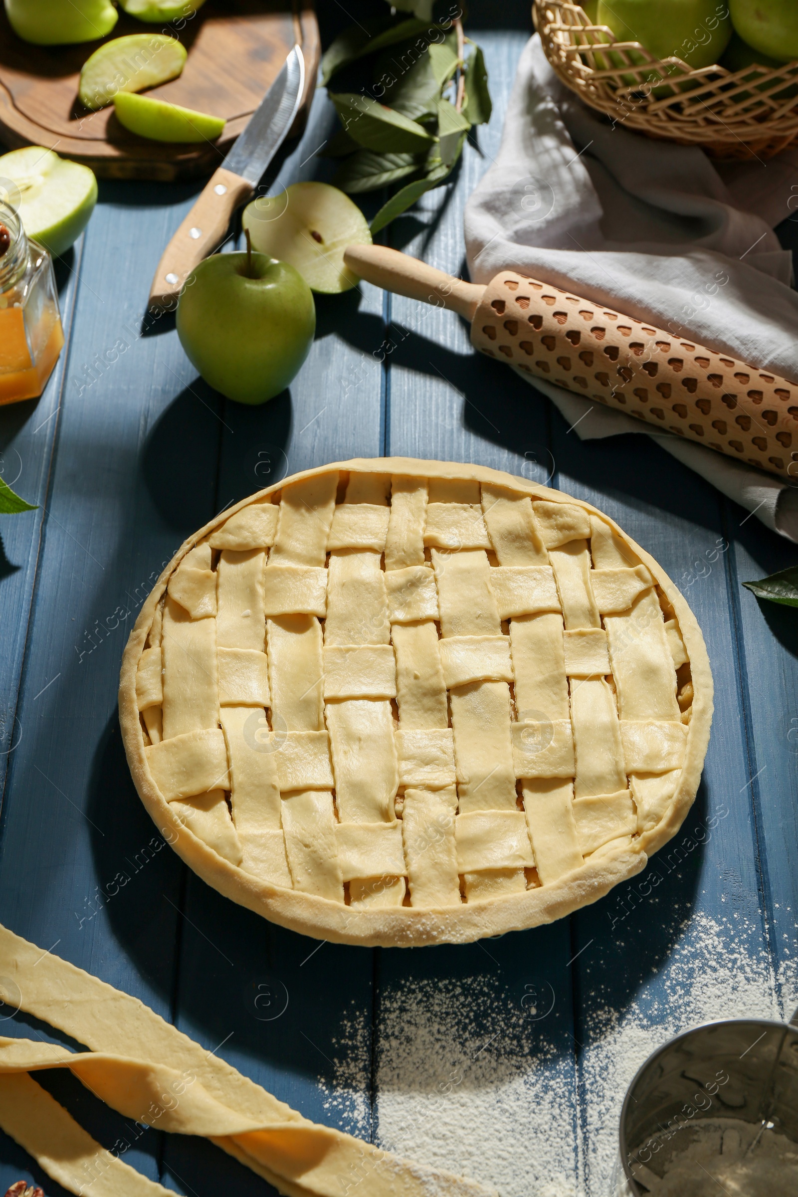 Photo of Uncooked homemade apple pie and ingredients on blue wooden table