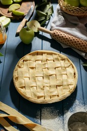 Photo of Uncooked homemade apple pie and ingredients on blue wooden table