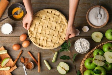 Photo of Woman making homemade apple pie and ingredients on wooden table, top view