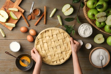 Photo of Woman making homemade apple pie and ingredients on wooden table, top view