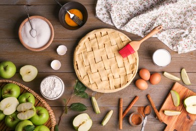 Photo of Uncooked homemade apple pie and ingredients on wooden table, flat lay