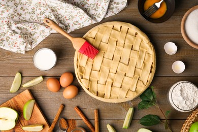 Photo of Uncooked homemade apple pie and ingredients on wooden table, flat lay