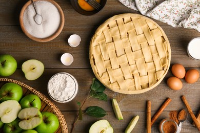 Photo of Uncooked homemade apple pie and ingredients on wooden table, flat lay