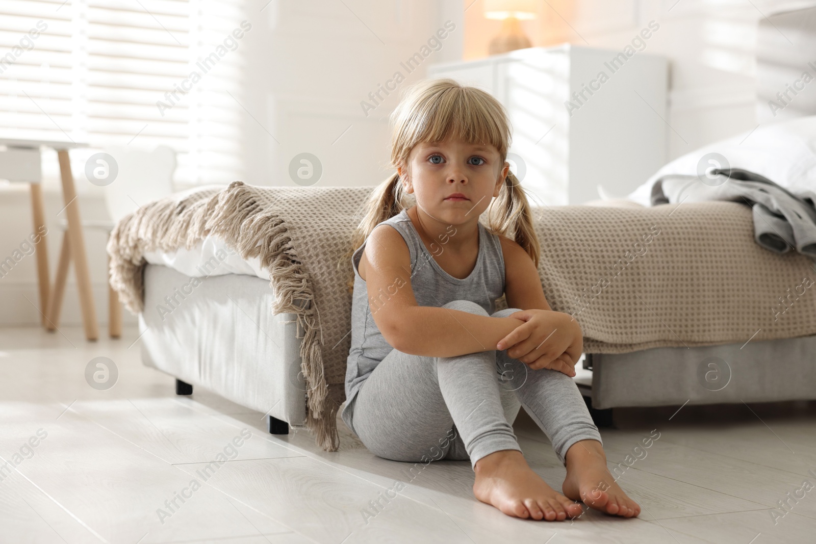 Photo of Orphanage concept. Sad little girl sitting on floor in child`s room