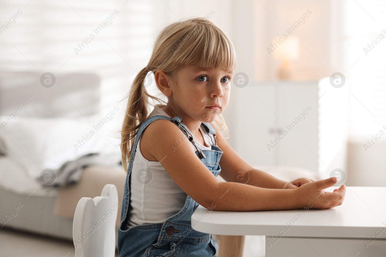 Photo of Orphanage concept. Sad little girl at table indoors