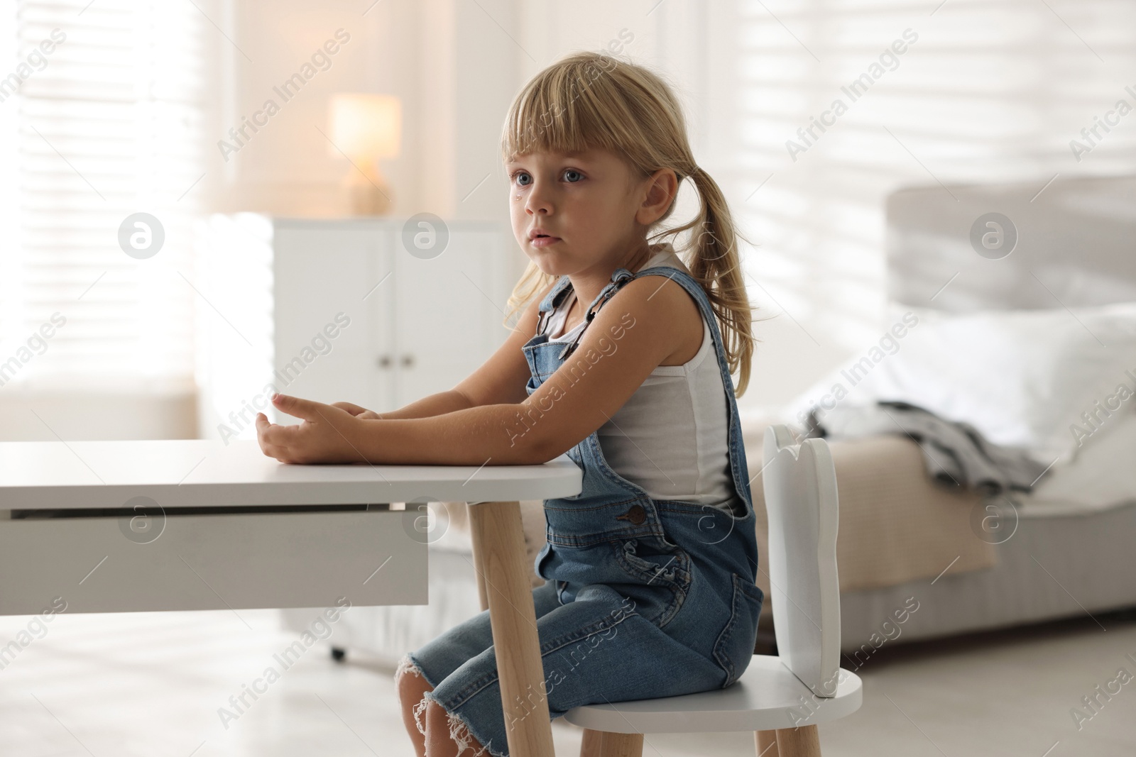 Photo of Orphanage concept. Sad little girl at table indoors