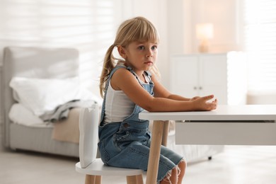 Photo of Orphanage concept. Sad little girl at table indoors