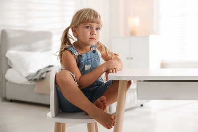 Photo of Orphanage concept. Sad little girl at table indoors