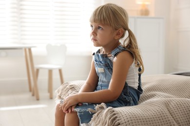 Photo of Orphanage concept. Sad little girl sitting on bed indoors, space for text