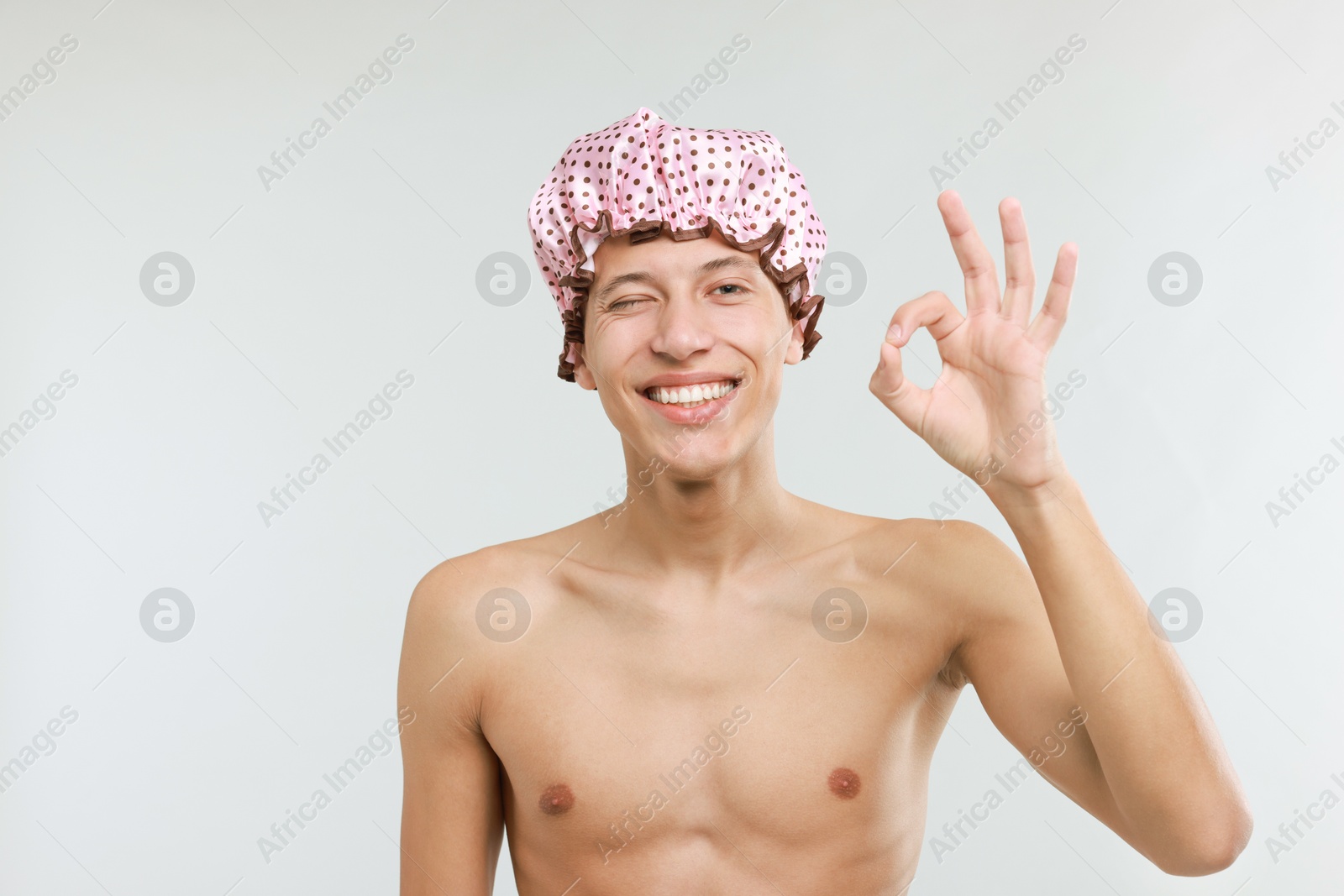 Photo of Man in shower cap showing ok gesture on light grey background