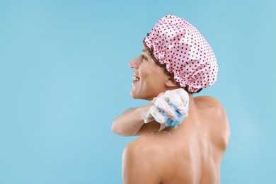 Photo of Man with shower cap and mesh sponge on light blue background, space for text