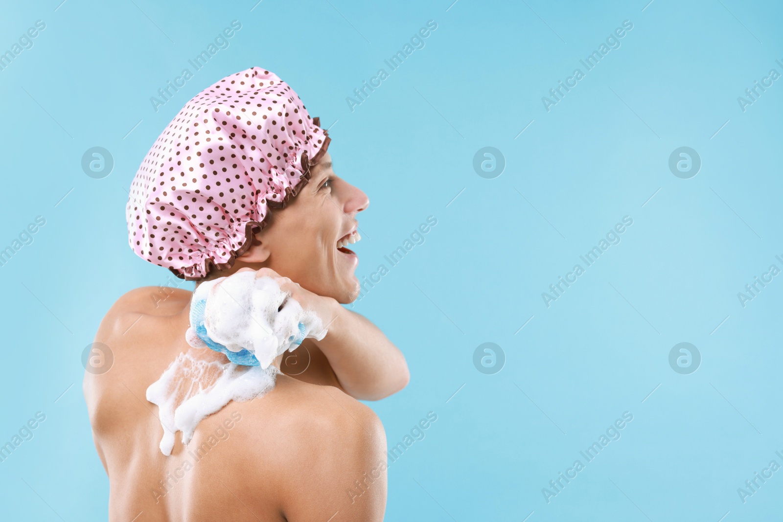 Photo of Man with shower cap and mesh sponge on light blue background, space for text