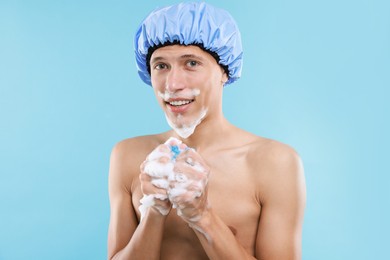 Photo of Man with shower cap and mesh sponge on light blue background