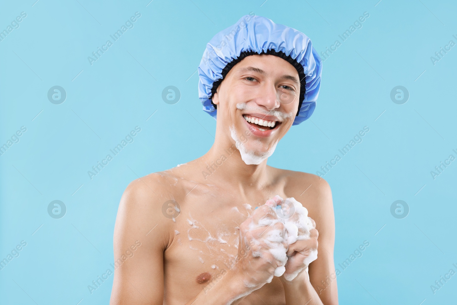 Photo of Man with shower cap and mesh sponge on light blue background