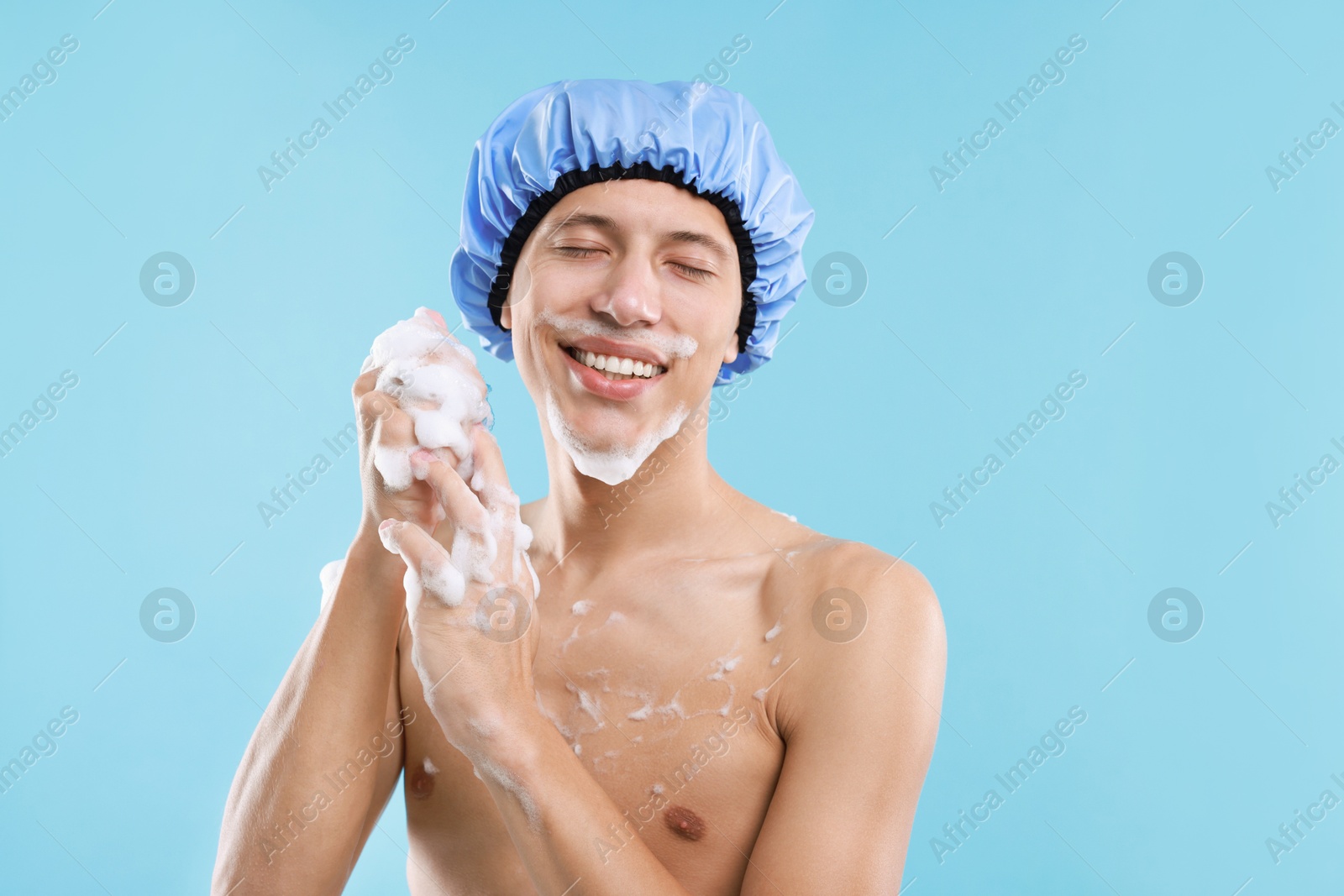 Photo of Man with shower cap and mesh sponge on light blue background