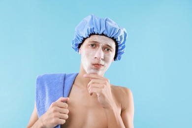 Photo of Man in shower cap with cream on his face against light blue background