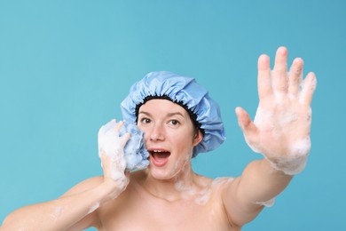 Photo of Emotional woman with shower cap and mesh sponge making stop gesture on light blue background