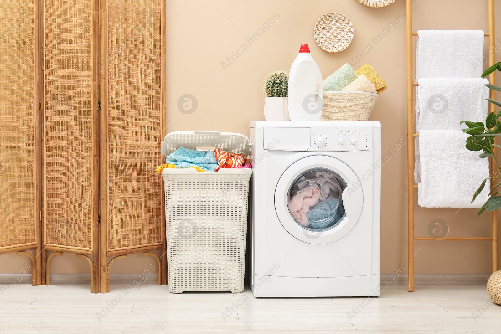 Photo of Wicker basket full of laundry, washing machine and detergent in bathroom