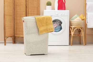 Photo of Wicker laundry basket with towel near washing machine in bathroom