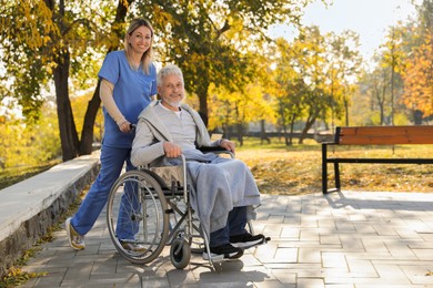 Photo of Caregiver assisting senior man on wheelchair in park, space for text. Home health care service