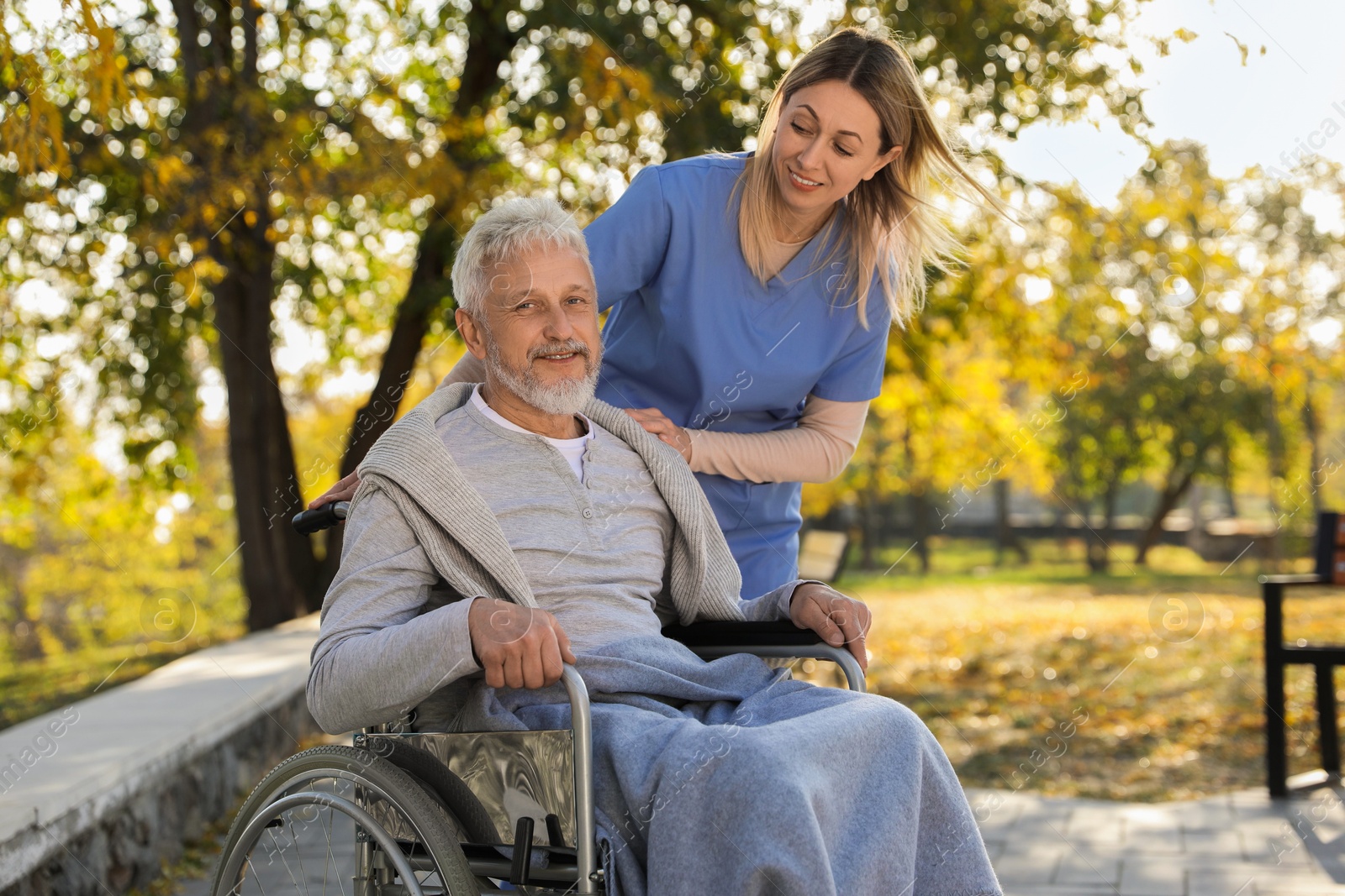 Photo of Caregiver assisting senior man on wheelchair in park. Home health care service